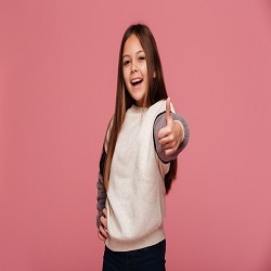 Happy brunette girl in casual showing thumbs up and smiling to camera isolated over pink